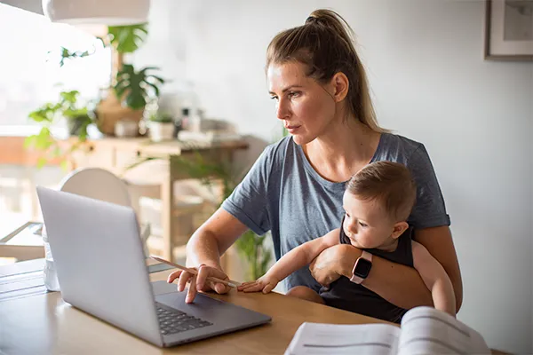 Stressed mother holding a baby looking at a laptop