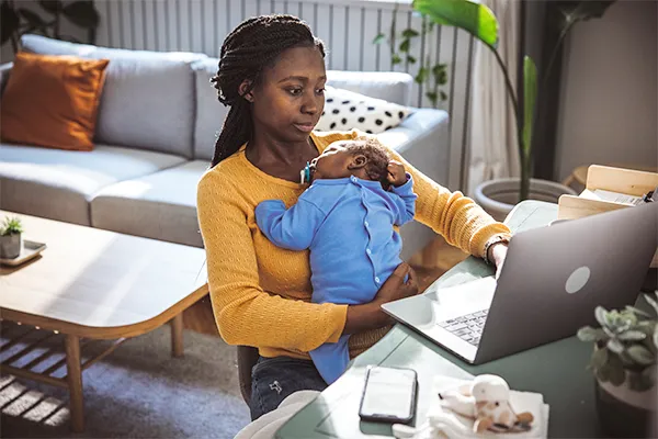 Mother holding infant messaging co-parent on a laptop