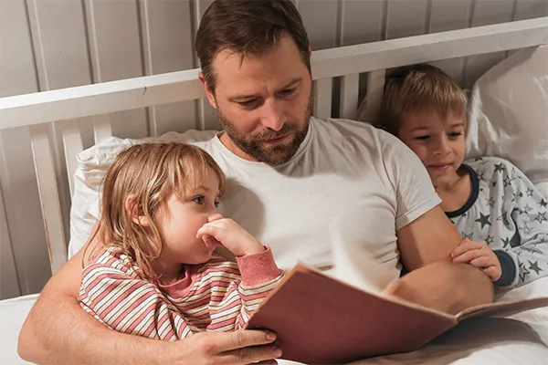 Father reading to son and daughter in bed
