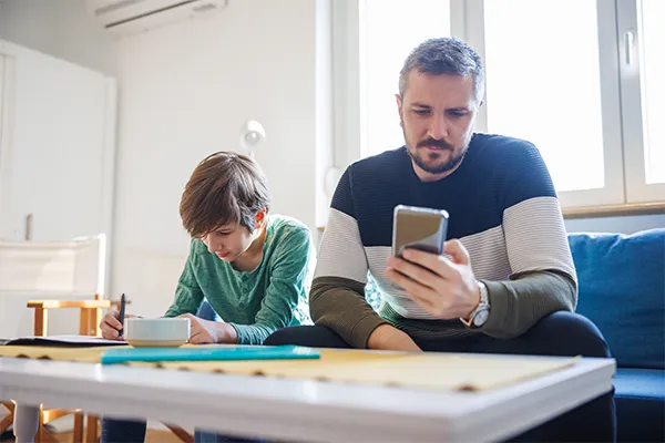 Father texting while sitting beside son