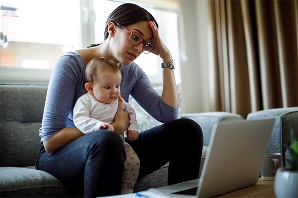 Frustrated mother holding infant looking at computer