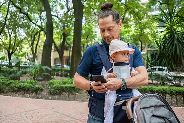 Father carrying baby loooking at phone