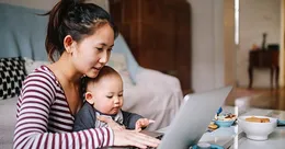 Mother holding baby while working on computer
