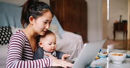 Mother holding baby while working on computer